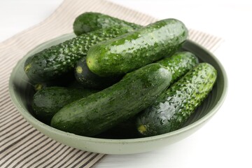 Fresh cucumbers in bowl on white wooden table, closeup