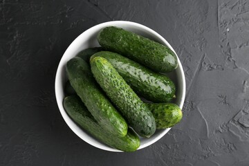 Fresh cucumbers in bowl on dark textured table, top view