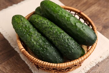 Fresh cucumbers in wicker basket on wooden table, closeup