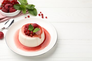 Delicious panna cotta with berries, sauce and mint on white wooden table, closeup. Space for text