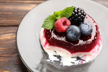 Delicious panna cotta with berries, jam and mint on wooden table, closeup