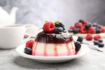 Tasty panna cotta with berries and jam on light grey table, closeup
