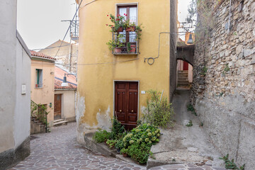 A small, charming yellow house with a traditional red roof, nestled in a narrow alley of an ancient Italian village.