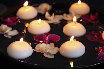 Burning candles and orchid flowers floating in water on plate, closeup