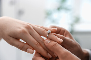 Making proposal. Man putting engagement ring on his girlfriend's finger indoors, closeup