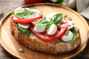 Delicious sandwich with mozzarella cheese, tomatoes and basil on wooden table, closeup