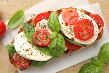 Delicious sandwich with mozzarella cheese, tomatoes and basil on wooden table, flat lay