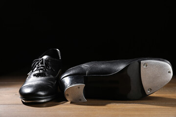 Pair of tap shoes on wooden floor against black background, closeup. Tap dance