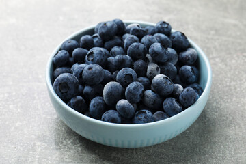 Ripe frozen blueberries in bowl on grey textured table, closeup