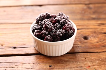 Ripe frozen blackberries in bowl on wooden table, closeup