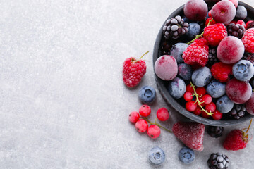 Mix of ripe frozen berries and bowl on grey textured table, flat lay. Space for text