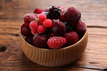 Mix of ripe frozen berries in bowl on wooden table, closeup