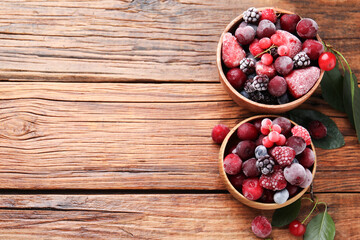 Mix of ripe frozen berries and green leaves on wooden table, flat lay. Space for text