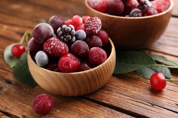 Mix of ripe frozen berries and green leaves on wooden table, closeup