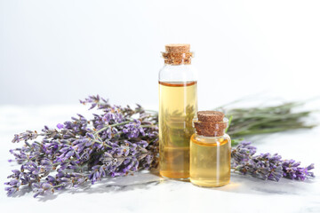 Aromatic essential oil in bottles and lavender flowers on white table against light grey background, closeup