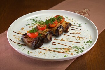 Grilled eggplant rolls stuffed with creamy filling, topped with cherry tomatoes, dill, and crushed nuts, drizzled with balsamic glaze.