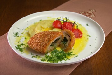 Crispy chicken Kyiv cutlet filled with herb butter, served with creamy potatoes, roasted cherry tomatoes, and garnished with fresh dill.