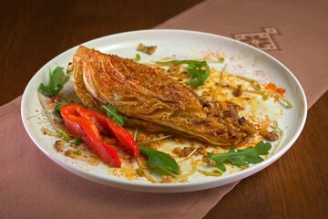 Roasted cabbage wedge with crushed nuts, herbs, and spices, served with bell pepper slices and fresh arugula on a white plate.