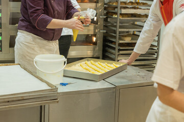 Baker preparing pastry dough in a commercial kitchen with trays and baking equipment visible