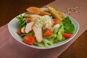 Fresh Caesar salad with grilled chicken, cherry tomatoes, quail eggs, parmesan shavings, and garlic croutons served in a white bowl.