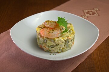 Traditional Olivier salad with shrimp, peas, and vegetables in mayonnaise dressing, elegantly plated in a white bowl.