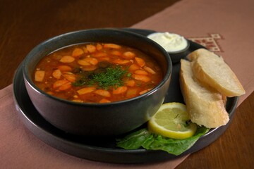 Traditional Russian solyanka soup with sausages, olives, lemon, and fresh dill, served with sour cream and crusty bread.