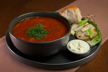 Traditional borscht soup served with sour cream, fresh dill, bread, and slices of pork with garlic and green onion garnish.