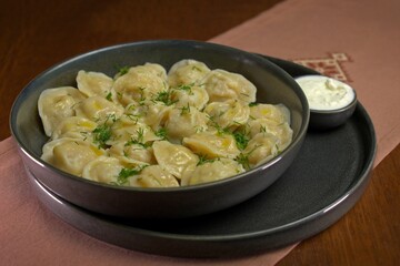 Traditional boiled dumplings garnished with fresh dill and served with sour cream in a dark ceramic bowl.