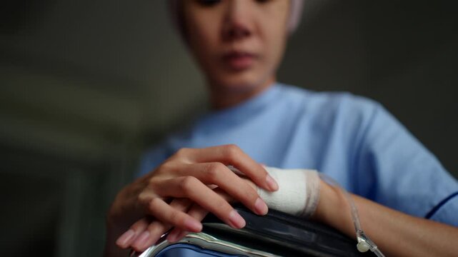 Close up at hand with intravenous saline injection of patient woman with cancer sitting on wheelchair suffering pain after chemotherapy at hospital, sickness alone female in headscarf feeling unwell.