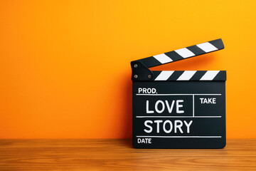 Naklejka premium Black movie clapperboard with LOVESTORY text on orange background and wooden surface