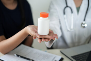 Doctor and patient together sitting in hospital clinic and holding a medicine bottle to assess the quality of medicine, recommending medication to patient and explaining the dose and description.