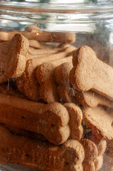 A close-up looking through the clear glass of a jar, filled with a pile of bone-shaped dog treats. The image highlights the rough, grainy texture of the biscuits and their layered arrangement.