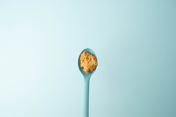 Blue spoon full of crunchy, creamy peanut butter over a blue background. Copy space.