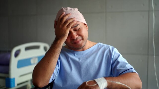 Depressed young patient man with cancer in headscarf feeling stressed and hopeless while sitting alone on wheelchair in the hospital room, mental health and disease awareness on world cancer day.