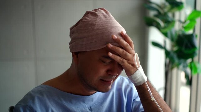 Depressed young patient man with cancer in headscarf feeling stressed and hopeless while sitting alone on wheelchair in the hospital room, mental health and disease awareness on world cancer day.