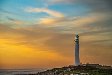 Scenic lighthouse at sunset with warm golden light, dramatic clouds, and a tranquil ocean horizon. Perfect for travel, tourism, and maritime themes, with ample copy space for text placement. Ideal as 