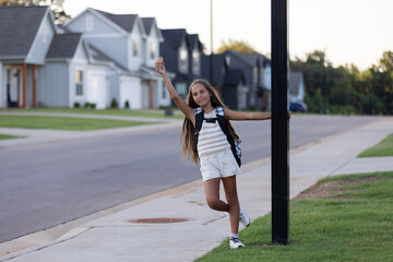 Happy young girl with backpack, holding an ice cream in her hand while standing playfully on a suburban street.