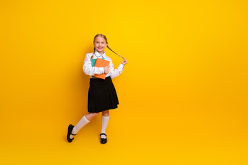 Smiling schoolgirl in uniform holding book on yellow background promoting education and back to school concepts