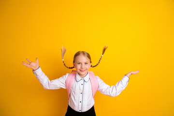 Joyful schoolgirl with braids wearing a formal white shirt and pink backpack gesturing cheerfully on a yellow background