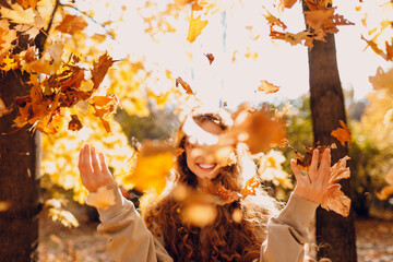 Smiling young woman throw up the autumn leaves in the forest at sunset