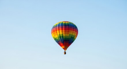 Fototapeta premium Rainbow striped hot air balloon floating in a clear blue sky image