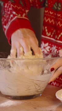 Vertical video. Woman in Festive Sweater Kneading Dough in Glass Bowl Beside Sifter and Flour in Cozy Kitchen with Christmas Tree in Frame