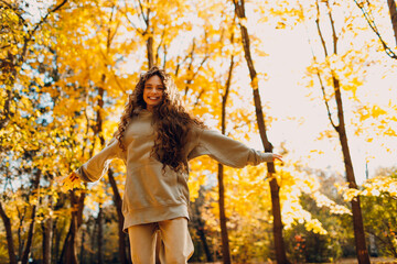 Smiling young woman plays and jumping dancing in the autumn forest with the yellow leaves at sunset
