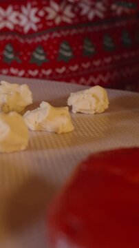Vertical video. Close Up of Cookie Dough Balls and Red Dough on Baking Sheet While Woman in Sweater Prepares in Background