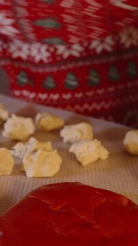 Vertical video. Woman in Red Christmas Sweater Picking Up Raw Dough Pieces from Parchment Sheet in Warm Kitchen Lighting