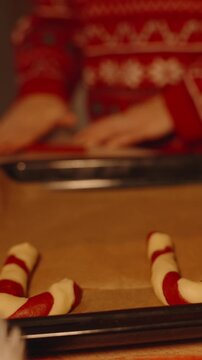Vertical video. Spiral Candy Cane Cookies on Tray While Woman in Christmas Sweater Shapes More in Background beside Decorated Tree