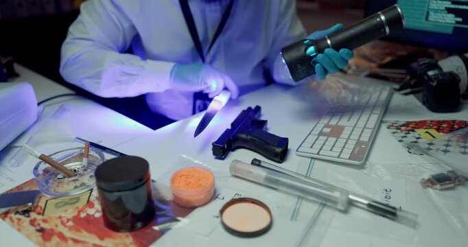 Hands, forensics and evidence at lab for weapon inspection with uv light, knife and gun for proof. Person, torch and investigation with tools for lead, crime and police examination for fingerprints