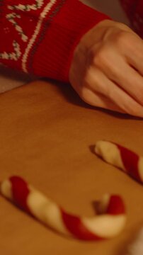 Vertical video. Woman Placing Candy Cane Shaped Dough on Baking Paper Near Christmas Tree and Red Santa Hat in Warm Lighting