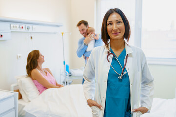 Fototapeta premium Confident Female Doctor in Scrubs with Patient Family in Bright Hospital Room