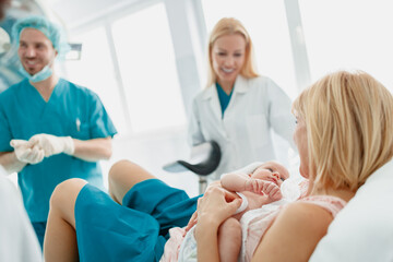 New Mother Holding Newborn with Supportive Medical Team in a Well-Lit Hospital Room